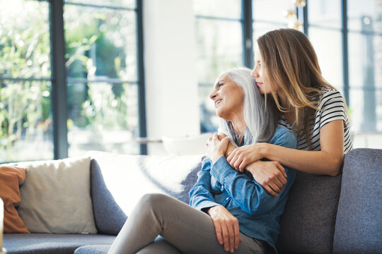 Daughter holding mother in her arms, sitting on couch