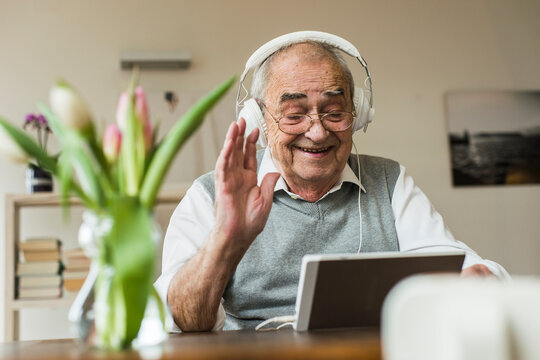 Senior man using mini tablet and headphones for skyping at home