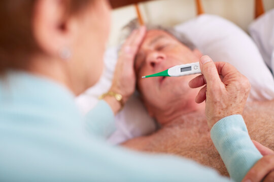 Senior woman taking temperature of sick husband at home
