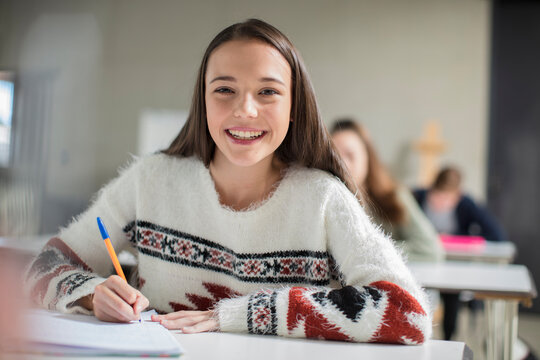 Portrait of smiling teenage girl writing in exercise book in class