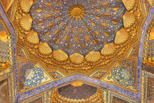 Gilded dome interior of Ak Saray Mausoleum in Samarkand with intricate muqarnas and floral patterns in gold and blue. Ideal for travel publications, cultural heritage articles, and architectural.