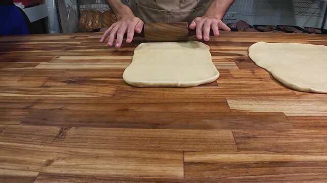 Close-up of a baker's hands skillfully using a wooden rolling pin, flattening smooth dough for traditional recipes in an authentic culinary workshop.
