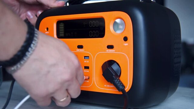 Man plugging cable into portable power station. Rechargeable battery device for emergency electricity and camping. Sustainable energy solution for off-grid power supply.