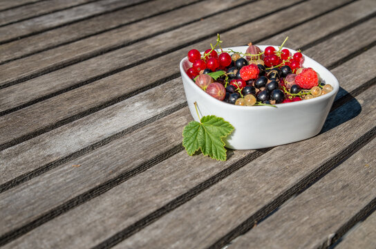 A white dish with a mix of fresh berries right side on wooden table, leaf decorating the dish