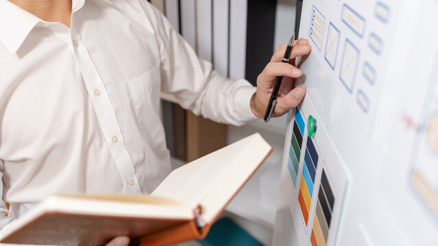 Close-up of a UX designer reviewing wireframes, interface layouts, and visual design elements on a planning board for user interface development, usability testing, and digital product design.