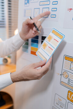 Close-up of a UX designer reviewing wireframes, interface layouts, and visual design elements on a planning board for user interface development, usability testing, and digital product design.
