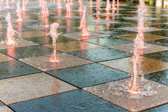 Pink tinted water jets in urban square fountain