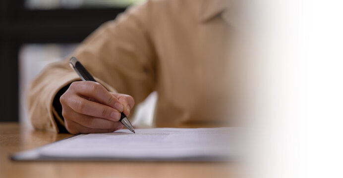 person signing or writing on a document with a pen at a desk business agreement paperwork education