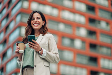 Happy young woman laughing, holding coffee and mobile phone, enjoying city life and communicating