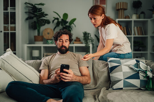 Couple having conflict over phone addiction, woman frustrated with man ignoring her for smartphone at home