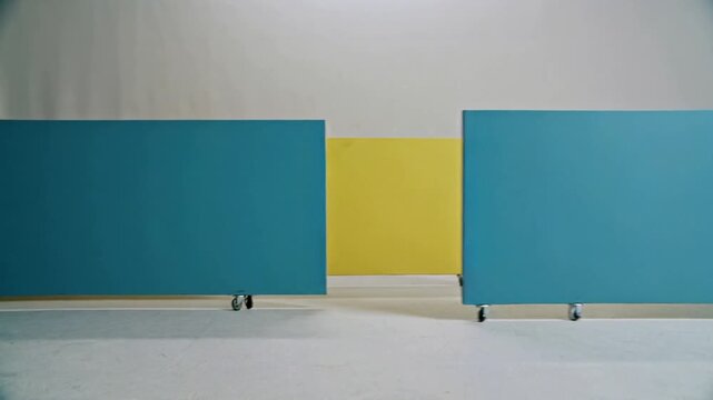 Sliding teal, red, yellow panels across studio as casters roll, rearranging order to center yellow