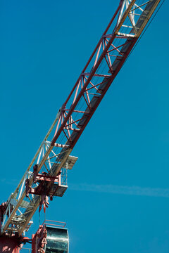 The long steel jib of a tower crane stretches diagonally across a clear blue sky over a city construction site.