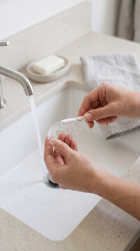 Woman washing transparent occlusal splint (night guard) under faucet in bathroom sink, close-up