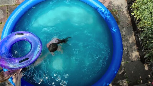 Mother daughter cooling. Home inflatable pool helping family survive extreme summer heat. Backyard swimming during heatwave reflecting global warming, critically high temperatures, climate change