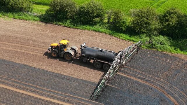 Precision nutrient application tractor distributing liquid organic fertilizer on cultivated farmland. Soil conditioning workflow supporting regenerative agriculture, crop yield improvement, efficient