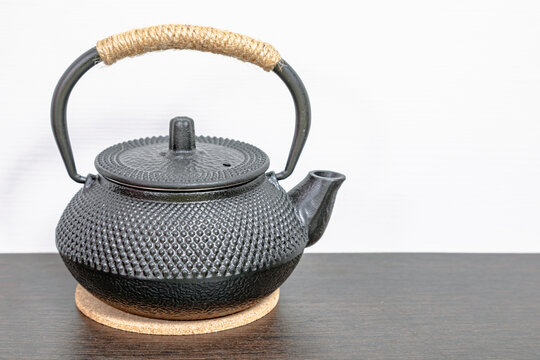 Black cast iron teapot for brewing matcha tea. Traditional oriental vessel with textured surface and rustic handle on wooden table. Zen culture and healthy lifestyle concept