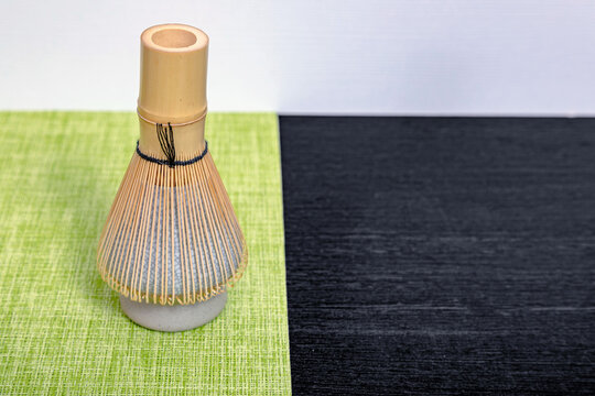 Bamboo matcha whisk resting on a ceramic holder. Traditional Japanese tea preparation tool on a textured table. Ceremony utensil for whisking green powder for health beverage