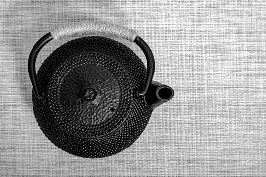Black cast iron teapot on a textured mat. Traditional Japanese tea set utensil for matcha preparation. Minimalist kitchen accessory for healthy beverage consumption and tea ceremony