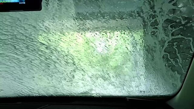  Point of view from inside vehicle during automated cleaning service. Automatic car wash process with water and foam spraying on windshield