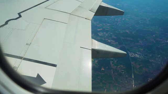 Plane flying above farmland and town clusters divided by roads, view from window porthole. Jet cruising over rural region with visible settlements and field patterns. Aircraft gliding across