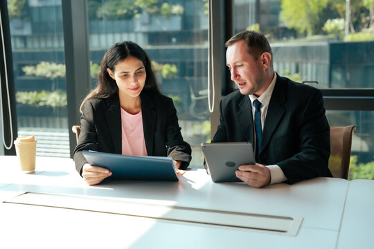 Business professionals discuss project details while comparing tablet with printed documents inside modern office. Corporate communication, teamwork, planning, strategy, management, collaboration.