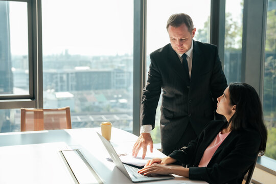 Business manager discussing project details with employee using laptop during office meeting. Corporate teamwork focuses on workflow improvement and solving business challenges.