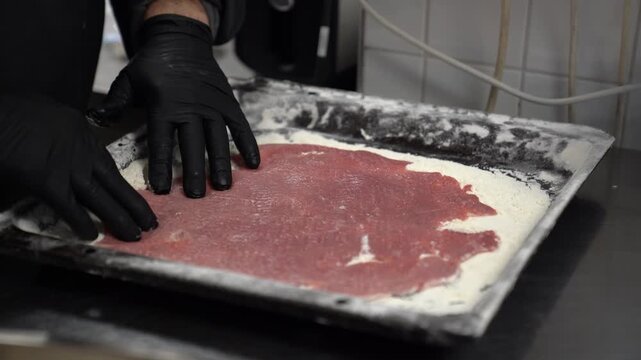 Male cook wearing black gloves preparing a cutlet for frying in a restaurant kitchen setting