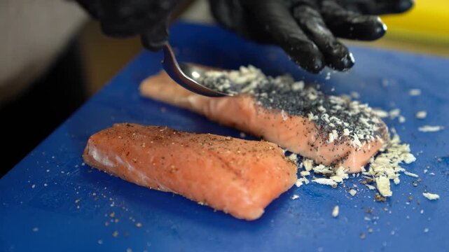 Chef preparing salmon fillet with poppy seeds and parmesan cheese for grilling