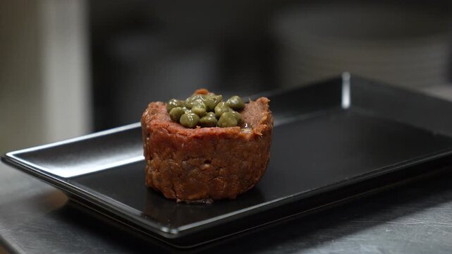 Culinary expert garnishing a fresh beef tartare with capers on a stylish black plate
