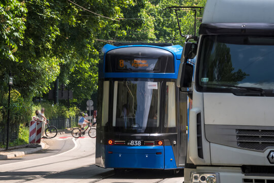 Polska, Krak&oacute;w, 24 maja 2026, 13:05. Ciężar&oacute;wka Renault i niebieski tramwaj nr 8 poruszają się po bujnej, wysadzanej drzewami ulicy w Krakowie. W tle widać rowerzyst&oacute;w, cieszących się wiosennym dniem.