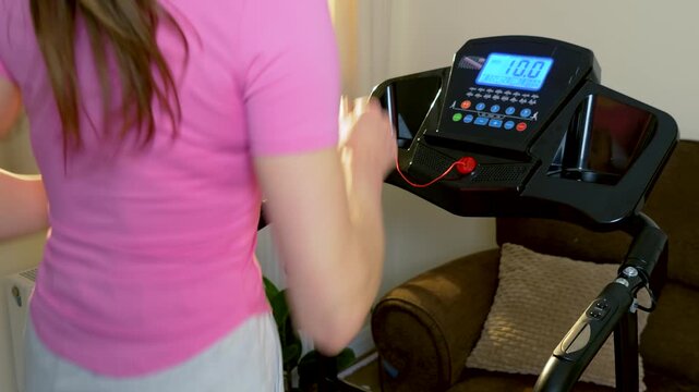 Unrecognizable woman jogging on treadmill with digital control panel in apartment. Indoor cardio training and steady running pace during everyday home fitness routine. Active healthy lifestyle through