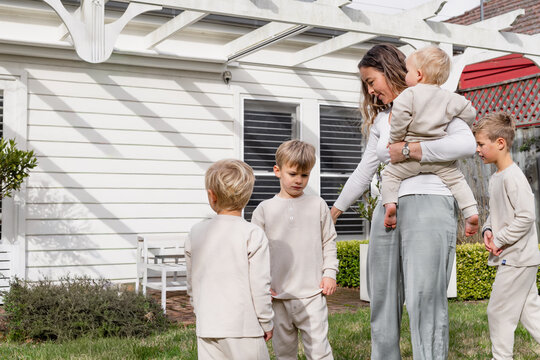 young boys standing in the backyard with mum holding a baby on her hip