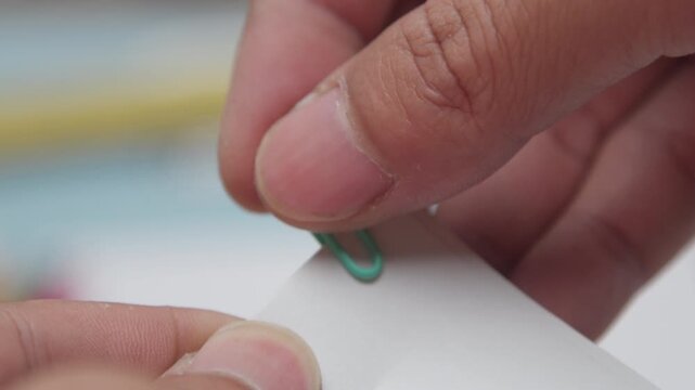 Close Up of Hands Attaching a Paper Clip to White Paper, Showcasing Back to School, School Supplies, Office Stationery, Organization, and Document Management