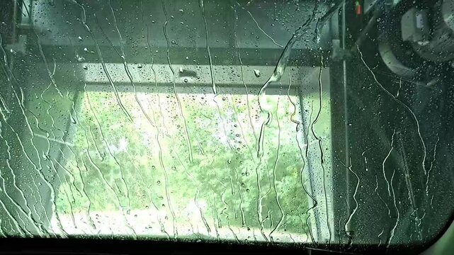 Water spray rinsing windshield glass in robotic cleaning station. Seen from inside a vehicle.
