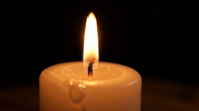 Close-up of a lit white pillar candle with a warm glowing flame, creating a peaceful and serene ambiance for relaxation, meditation, or special occ...