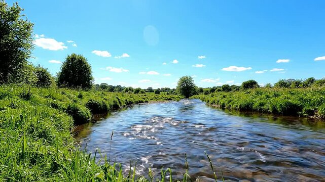 Serene River Flowing Through Lush Green Countryside Under Bright Blue Summer Sky with Fluffy Clouds, Natural Landscape for Outdoor Recreation and R...