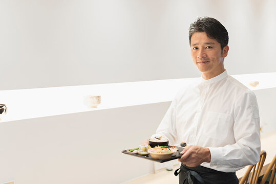 和食ランチプレートを配膳する笑顔の40代男性カフェ店員