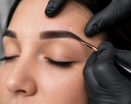 Beauty specialist shaping eyebrow with tweezers close up