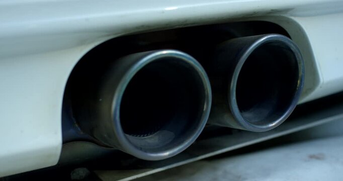 Close-up view of twin exhaust tailpipes integrated into the rear bumper of a white sports car