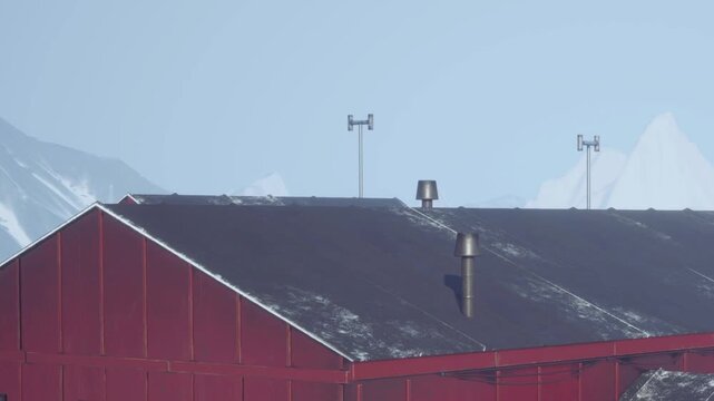 A red building stands against a clear sky. Wind gauges and antennas are on the roof. Snow covers parts of the structure. This scene shows winter weather conditions.