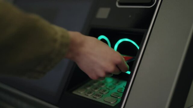 Close-up of a person's hand inserting a red credit card into an automated teller machine slot to withdraw money, a modern banking technology concept for financial transactions