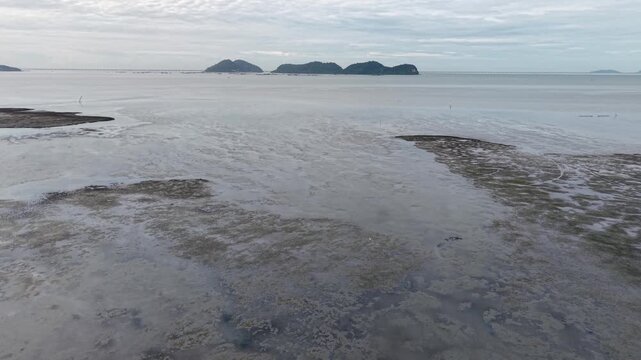 Aerial footage of coastal mudland exposed at low tide with distant islands.