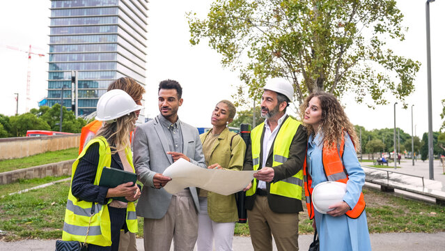 Multi ethnic group of architects and engineers reviewing blueprints outdoors, planning a new building project in the city