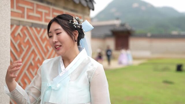 Young woman in traditional Korean attire smiles gently. Her gaze turns toward the horizon, reflecting calm contemplation. Background shows ancient brick walls with intricate patterns