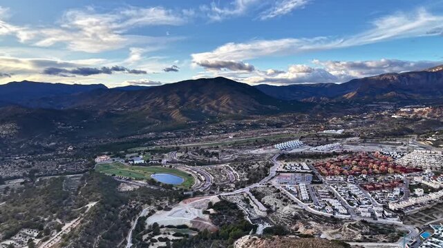 Aerial mountain valley suburb at dusk, drone operator surveying residential development, winding roads, water