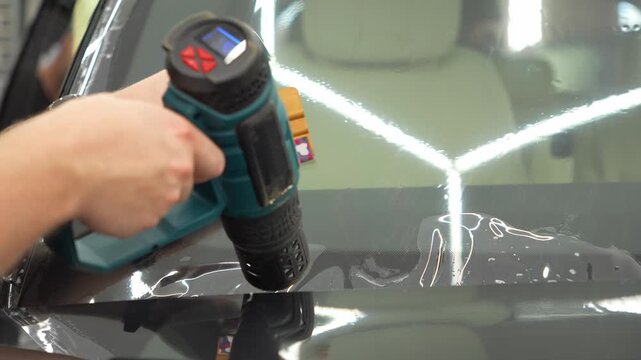 Athermal film on the windshield of the car. Car wrapping. Windshield protection. A man in the process of tinting the windshield. The concept of love for cars protection. The process of installing PPF.