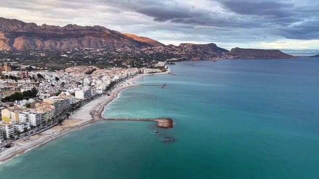 Wide coastal panorama rocky breakwater sunrise glow, slow drone reveal of jagged rock formations