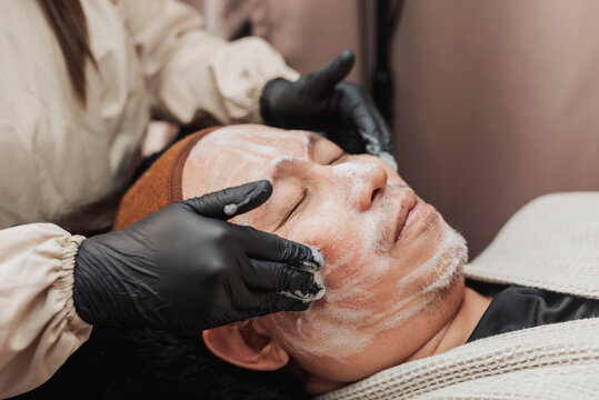 Professional esthetician cleansing a middle-aged man's face before hydradermabrasion treatment, removing impurities and preparing the skin for deep exfoliation and hydration.