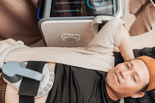 Relaxed middle-aged man comfortably undergoing Emsculpt HIFEM body contouring treatment on the abdomen, enjoying a non-invasive muscle toning session at a medical spa.