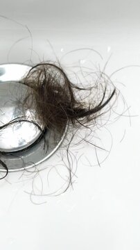 Hand pulls bun of female dirty hair from drain hole in bathroom. DIY drain clog cleaning shower drain hair loss stress, beriberi, alopecia. Clogged water drain in shower cabin, plumber clears blockage